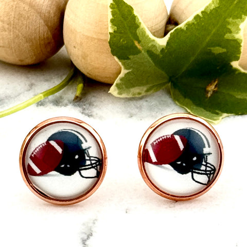 All Up In The Hair | Online Accessory Boutique Located in Mooresville, NC | Two Earrings featuring a cabochon with a black football helmet and football on a white marble background. Behind the earrings is a wood bead garland and ivy leaves.