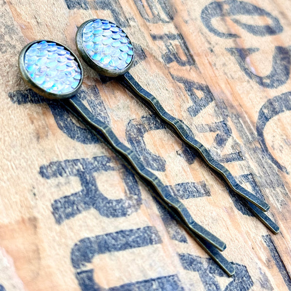 All Up In The Hair | Online Accessory Boutique Located in Mooresville, NC | Side view of two Frost Mermaid Bobby Pins laying on a wood background with black lettering.