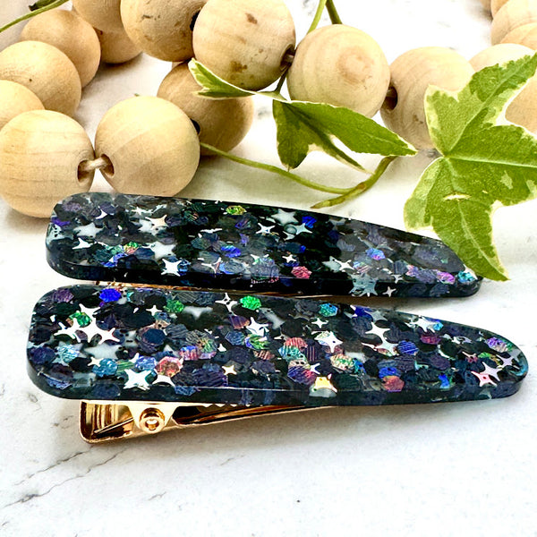 All Up In The Hair | Online Accessory Boutique Located in Mooresville, NC | Side view of our Galaxy Barrette Set on a white marble background. At the top of the image is a wood bead garland and ivy leaves.