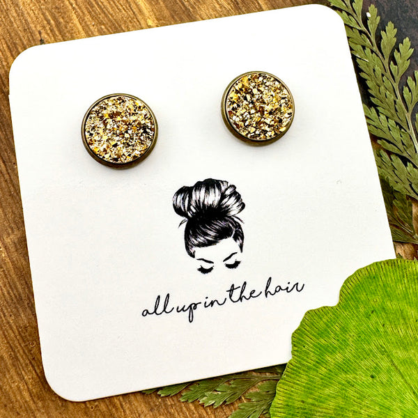 All Up In The Hair | Online Accessory Boutique Located in Mooresville, NC | Two gold druzy set in a bronze stud setting. The earrings are on a white, All Up In The Hair branded packaging card. The card is laying on a wood background, next to green leaves.