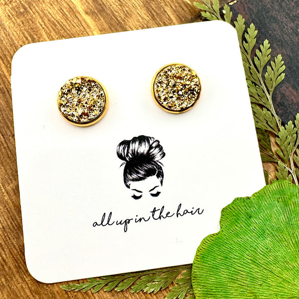 All Up In The Hair | Online Accessory Boutique Located in Mooresville, NC | Two gold druzy set in a gold stud setting. The earrings are on a white, All Up In The Hair branded packaging card. The card is laying on a wood background, next to green leaves.
