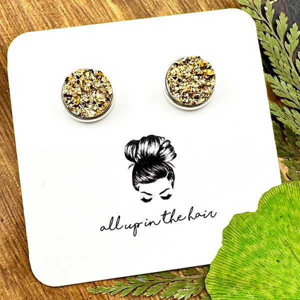 All Up In The Hair | Online Accessory Boutique Located in Mooresville, NC | Two gold druzy set in a silver stud setting. The earrings are on a white, All Up In The Hair branded packaging card. The card is laying on a wood background, next to green leaves.