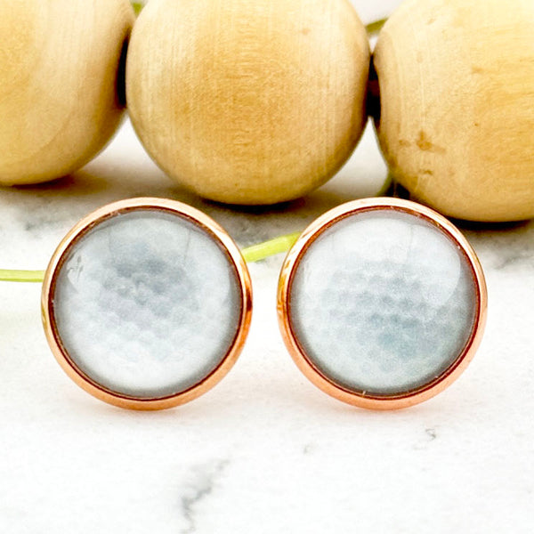 All Up In The Hair | Online Accessory Boutique Located in Mooresville, NC | Two Golf Ball Earrings laying on a white marble background. Behind the earrings is a wood bead garland and ivy leaves.