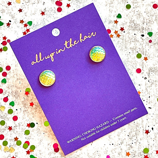 All Up In The Hair | Online Accessory Boutique Located in Mooresville, NC | Two green mermaid earrings on an All Up In The Hair branded packaging card. The card is laying on a gray background, surrounded by colorful glitter.