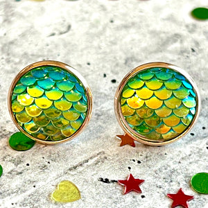All Up In The Hair | Online Accessory Boutique Located in Mooresville, NC | Two green mermaid earrings laying on a gray background, surrounded by colorful glitter.