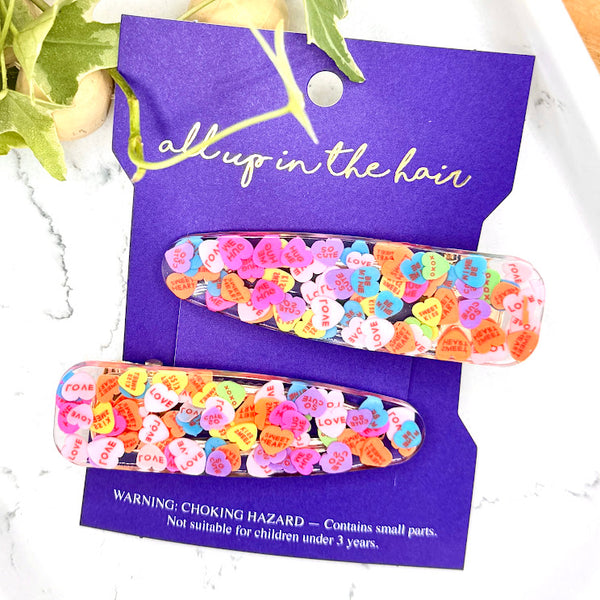 All Up In The Hair | Online Accessory Boutique Located in Mooresville, NC | Our Heart Barrette Set on an indigo colored, All Up In The Hair branded packaging card. The card is laying on a white background. At the top of the image is a wood bead garland and ivy leaves.