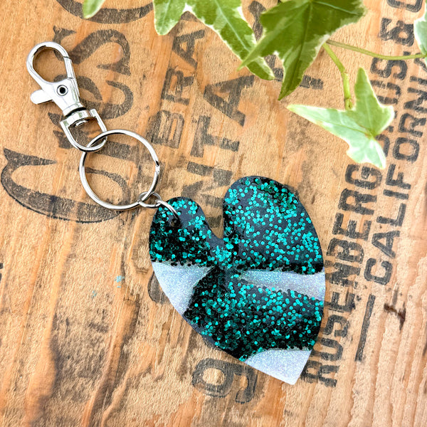 All Up In The Hair | Online Accessory Boutique Located in Mooresville, NC | Back of our Heart Leaf Albo Keychain on a wood background with black lettering. There are ivy leaves next to the keychain.