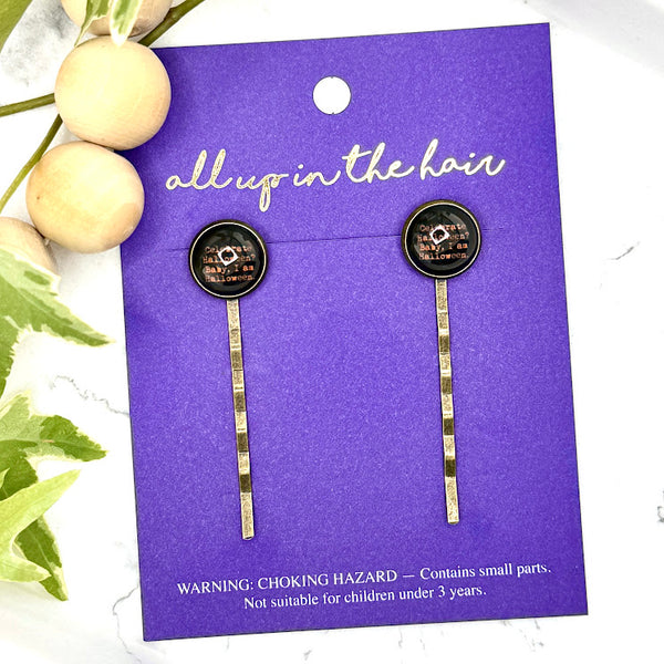 All Up In The Hair | Online Accessory Boutique Located in Mooresville, NC | Two I Am Halloween Bobby Pins on an indigo colored, All Up In The Hair branded packaging card. The card is laying on a white marble background next to a wood bead garland and ivy leaves.