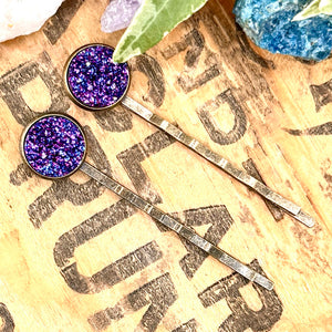 All Up In The Hair | Online Accessory Boutique Located in Mooresville, NC | Two Indigo Druzy Bobby Pins laying on a wood background with black lettering. There are crystals and ivy leaves at the top of the image.