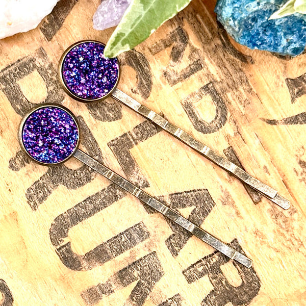 All Up In The Hair | Online Accessory Boutique Located in Mooresville, NC | Two Indigo Druzy Bobby Pins laying on a wood background with black lettering. There are crystals and ivy leaves at the top of the image.