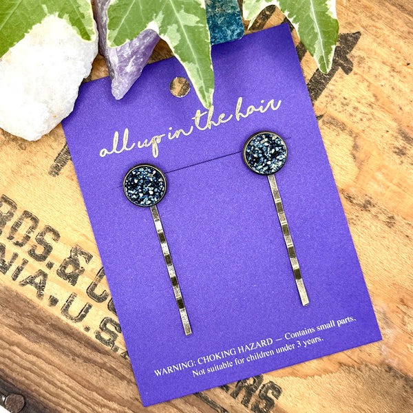 All Up In The Hair | Online Accessory Boutique Located in Mooresville, NC | An All Up In The Hair branded packaging card on a grey background, surrounded by colorful glitter. On the card is two labradorite druzy bobby pins.