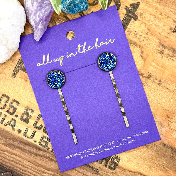 All Up In The Hair | Online Accessory Boutique Located in Mooresville, NC | Two Lapis Druzy Bobby Pins on an indigo colored, All Up In The Hair branded packaging card. The card is laying on a wood background with black lettering. There are ivy leaves and crystals at the top of the image.