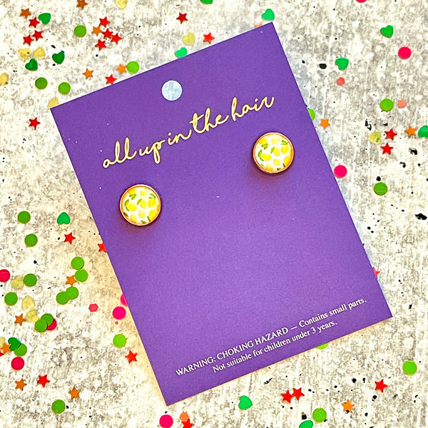 All Up In The Hair | Online Accessory Boutique Located in Mooresville, NC | Two lemon print earrings on an indigo colored, All Up In The Hair branded packaging card. The card is laying on a gray background, surrounded by colorful glitter.