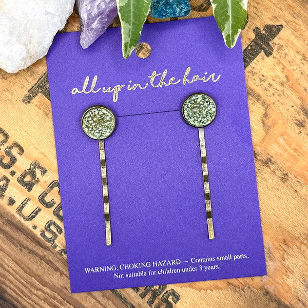 All Up In The Hair | Online Accessory Boutique Located in Mooresville, NC | Two Lemonade Druzy Bobby Pins on an indigo colored, All Up In the Hair branded packaging card. The card is laying on a wood background with black lettering. There are crystals and ivy leaves at the top of the image.