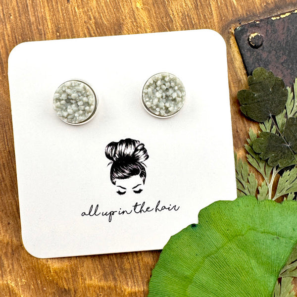 All Up In The Hair | Online Accessory Boutique Located in Mooresville, NC | Two light grey druzy cabochons in a silver setting on a white, All Up In The Hair branded packaging card. The card is laying on a wood background next to leaves.