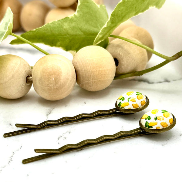 All Up In The Hair | Online Accessory Boutique Located in Mooresville, NC | Two Make Lemonade Druzy Bobby Pins laying on a white marble background with a wood bead garland and ivy leaves.