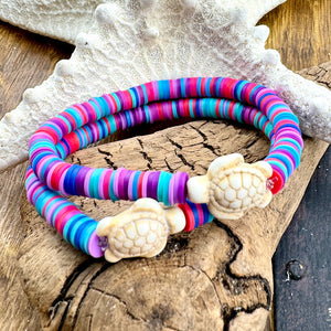 All Up In The Hair | Online Accessory Boutique Located in Mooresville, NC | Two vibrant teal and pink heishi bracelets with a white turtle beads laying on a piece of driftwood and a white starfish.