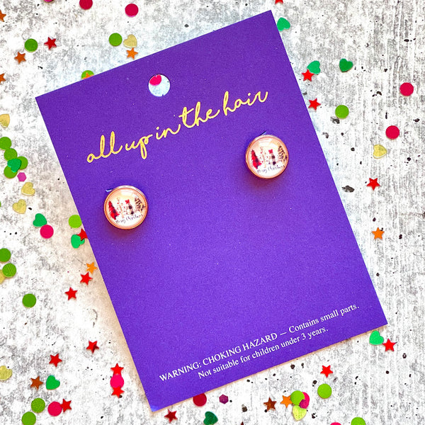 All Up In The Hair | Online Accessory Boutique Located in Mooresville, NC | Two Merry Christmas Stud Earrings on an indigo colored, All Up In The Hair branded packaging card. The card is laying on a gray background, surrounded by colorful glitter.