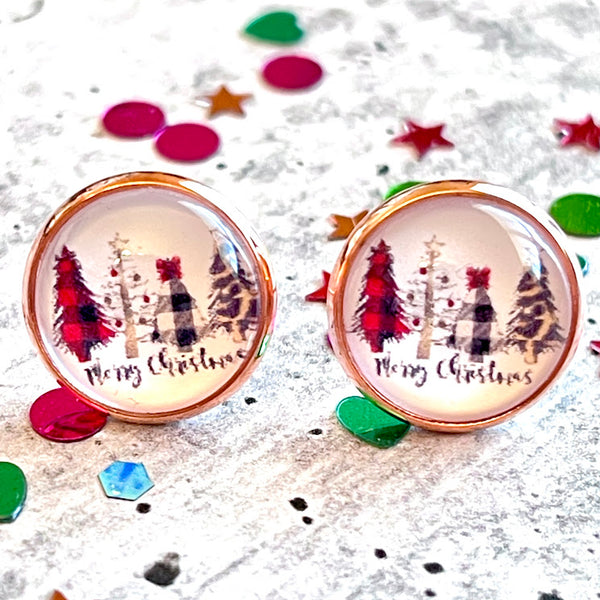All Up In The Hair | Online Accessory Boutique Located in Mooresville, NC | Close up of two stud earring with a white background and 4 different style christmas trees. Under the trees it says merry christmas in a handwritten font. The earrings are laying on a gray background, surrounded by colorful glitter.