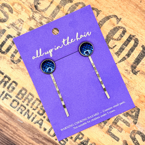 All Up In The Hair | Online Accessory Boutique Located in Mooresville, NC | Two Midnight Mermaid Bobby Pins on in indigo colored, All Up In The Hair branded packaging card. The card is laying on a wood background with black lettering.