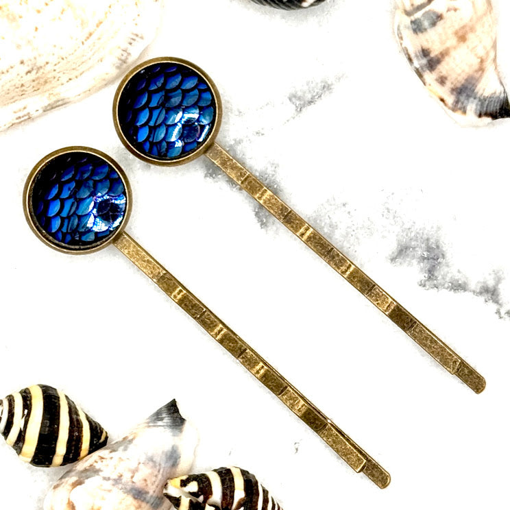 All Up In The Hair | Online Accessory Boutique Located in Mooresville, NC | Two midnight blue mermaid bobby pins laying diagonally on a grey background, surrounded by mermaid confetti.