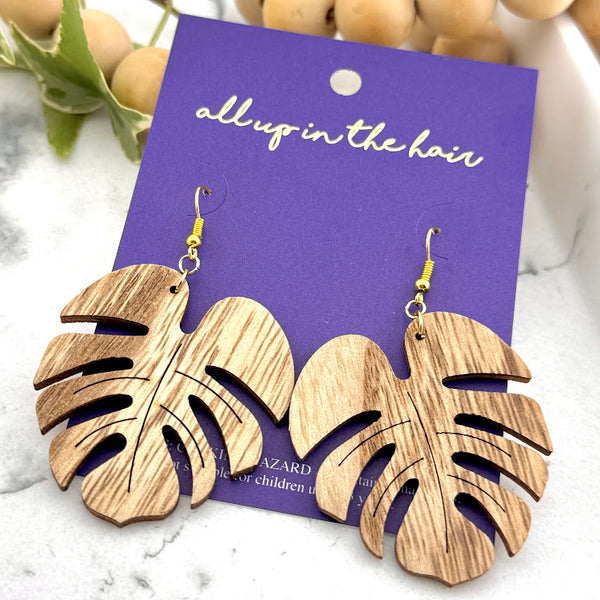 All Up In The Hair | Online Accessory Boutique Located in Mooresville, NC | Two Wood Monstera Earrings on an indigo colored, All Up In The Hair branded packaging card. The card is laying on a white marble background.