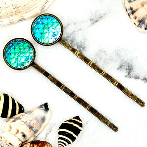 All Up In The Hair | Online Accessory Boutique Located in Mooresville, NC | Two Ocean Blue Mermaid Bobby Pins laying on a white marble background, surrounded by shells.