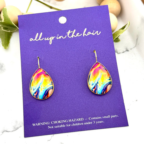 All Up In The Hair | Online Accessory Boutique Located in Mooresville, NC | Two Oil Slick Dangle Earrings on an indigo colored, All Up In The Hair branded packaging card. The card is laying on a white marble background alongside a wood bead garland and ivy leaves.