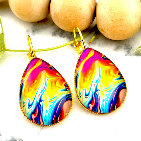 All Up In The Hair | Online Accessory Boutique Located in Mooresville, NC | Two Oil Slick Teardrop Dangle Earrings on a white marble background. Behind the earrings is a wood bead garland and ivy leaves.