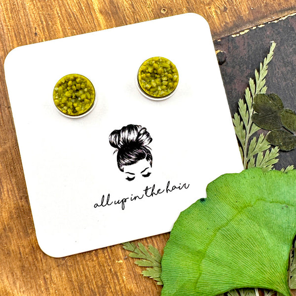 All Up In The Hair | Online Accessory Boutique Located in Mooresville, NC | Two Olivine Druzy Earrings in a silver setting on a white All Up In The Hair branded packaging card. The card is laying on a wood background with leaves next to it.