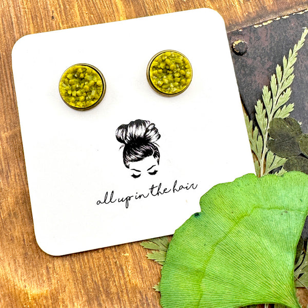 All Up In The Hair | Online Accessory Boutique Located in Mooresville, NC | Two Olivine Druzy Earrings in a bronze Setting on a white All Up In The Hair branded packaging card. The card is laying on a wood background with leaves next to it.