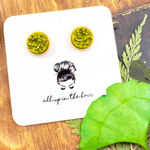 All Up In The Hair | Online Accessory Boutique Located in Mooresville, NC | Two Olivine Druzy Earrings in a Gold Setting on a white All Up In The Hair branded packaging card. The card is laying on a wood background with leaves next to it.