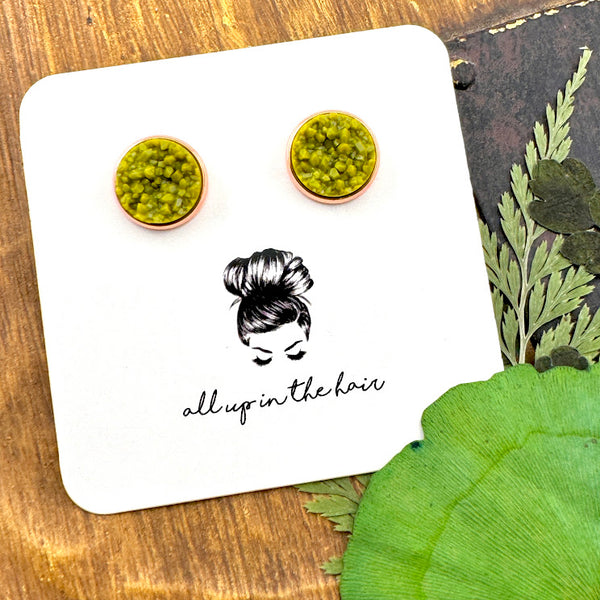 All Up In The Hair | Online Accessory Boutique Located in Mooresville, NC | Two Olivine Druzy Earrings in a rose gold Setting on a white All Up In The Hair branded packaging card. The card is laying on a wood background with leaves next to it.