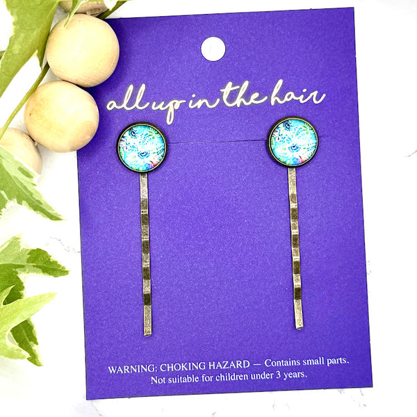 All Up In The Hair | Online Accessory Boutique Located in Mooresville, NC | Two Passionflower Bobby Pins on an indigo colored, All Up In The Hair branded packaigng card. The card is laying on a white marble background with wood bead garland and ivy leaves.