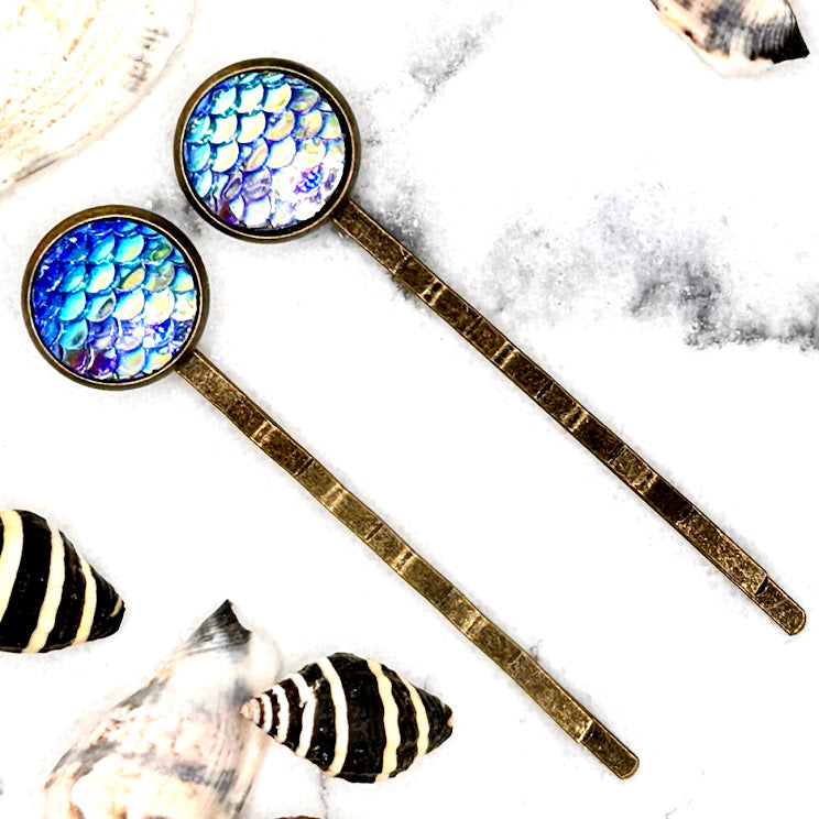 All Up In The Hair | Online Accessory Boutique Located in Mooresville, NC | Two Periwinkle Mermaid Bobby Pins laying on a white marble background, surrounded by shells.