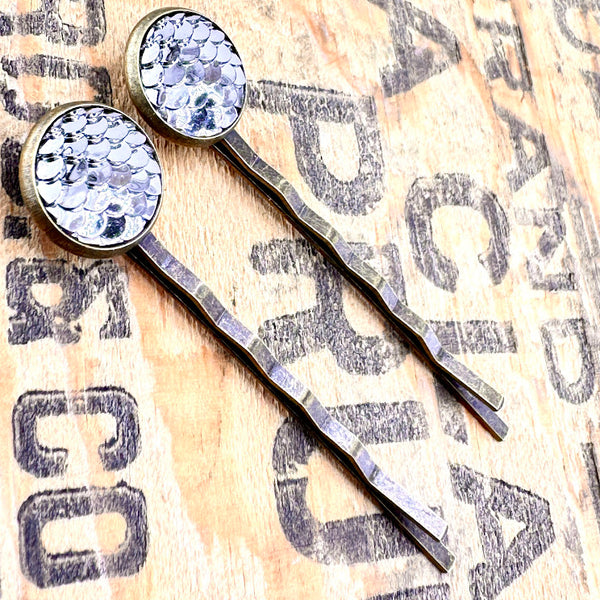 All Up In The Hair | Online Accessory Boutique Located in Mooresville, NC | Side view of two Pewter Mermaid Bobby Pins laying on a wood background with black lettering.