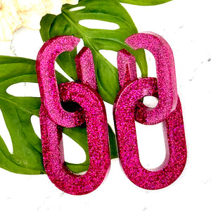 All Up In The Hair | Online Accessory Boutique Located in Mooresville, NC | Two Pink Chunky Chain Earrings laying on two monstera leaves. The leaves are laying on a white background.