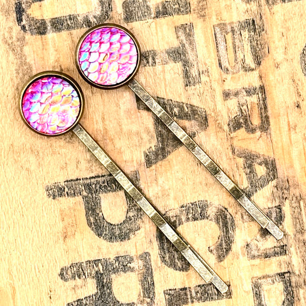 All Up In The Hair | Online Accessory Boutique Located in Mooresville, NC | Two Pink Mermaid Bobby Pins laying on a wood background with black lettering.