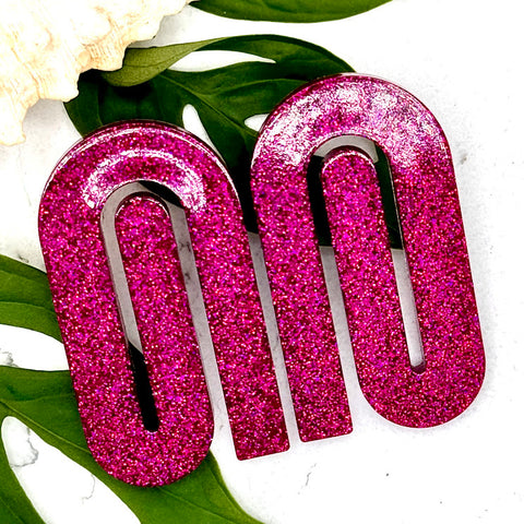 All Up In The Hair | Online Accessory Boutique Located in Mooresville, NC | Two Bright Pink Paperclip Earrings laying on a white background. Behind the earrings are some monstera leaves and a shell.