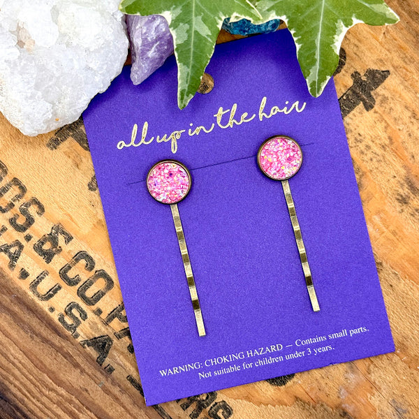 All Up In The Hair | Online Accessory Boutique Located in Mooresville, NC | Two Pink Topaz Druzy Bobby Pins on an indigo colored, All Up In The Hair branded packaging card. The card is laying on a wood background with black lettering. There are crystals and ivy leaves at the top of the image.