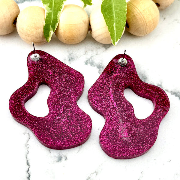 All Up In The Hair | Online Accessory Boutique Located in Mooresville, NC | Back of two Pink Wave Earrings on a white marble background. There is a wood bead garland and ivy leaves behind the earrings.