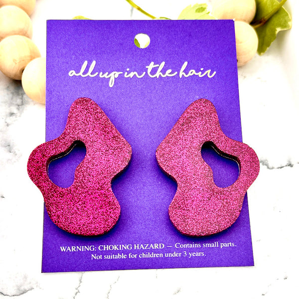 All Up In The Hair | Online Accessory Boutique Located in Mooresville, NC | Two Pink Wave Earrings on an indigo colored, All Up In The Hair branded packaging card. The card is laying on a white marble background.