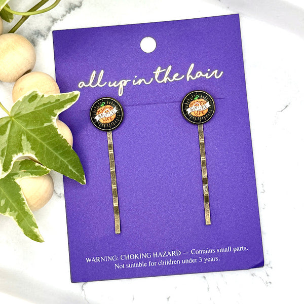 All Up In The Hair | Online Accessory Boutique Located in Mooresville, NC | Two Pumpkin Spice Life Bobby Pins on an indigo colored, All Up In The Hair branded packaging card. The card is laying on a white marble background next to a wood bead garland and ivy leaves.