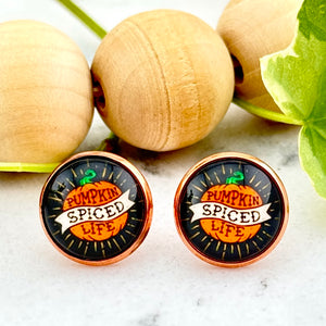 All Up In The Hair | Online Accessory Boutique Located in Mooresville, NC | Two round black earrings with a pumpkin with a banner in the center. The earrings say pumpkin spiced life. There is a wood bead garland and ivy leaves behind the earrings.