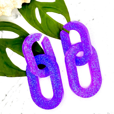 All Up In The Hair | Online Accessory Boutique Located in Mooresville, NC | Two Purple Chunky Chain Earrings laying on two monstera leaves on a white marble background.