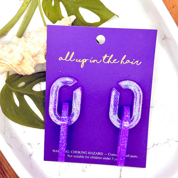 All Up In The Hair | Online Accessory Boutique Located in Mooresville, NC | Two Purple Chain Earrings on an indigo backer card. The card is laying on two monstera leaves on a white marble background.