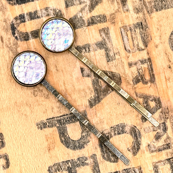 All Up In The Hair | Online Accessory Boutique Located in Mooresville, NC | Two Purple Mermaid Bobby Pins laying on a wood background with black lettering.