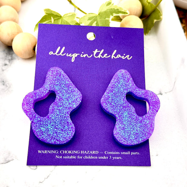 All Up In The Hair | Online Accessory Boutique Located in Mooresville, NC | Two Purple Wave Earrings on an indigo colored, All Up In The Hair branded packaging card. The card is laying on a white marble background.