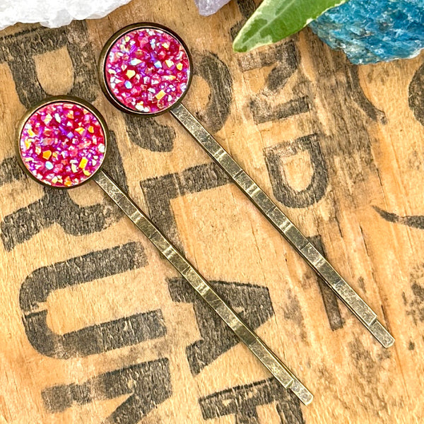 All Up In The Hair | Online Accessory Boutique Located in Mooresville, NC | Two strawberry red druzy bobby pins laying diagonally on a wood background with black lettering. There are crystals and ivy leaves at the top of the image.