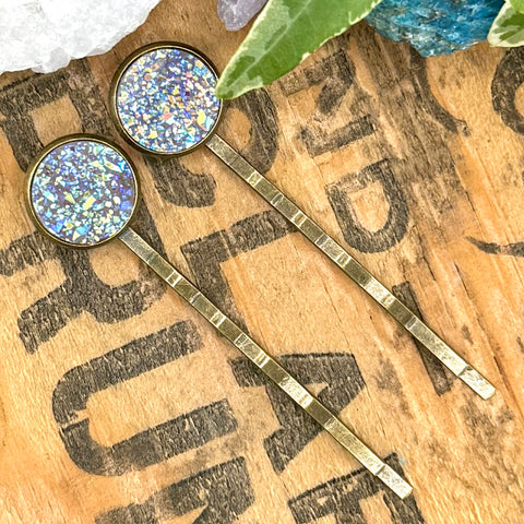 All Up In The Hair | Online Accessory Boutique Located in Mooresville, NC | Two delicate pink druzy bobby pins laying on a wood background with black lettering. There are crystals and ivy leaves at the top of the image.